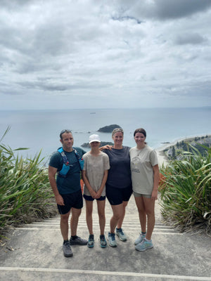 Four people standing on a road with a scenic background of sky and greenery.